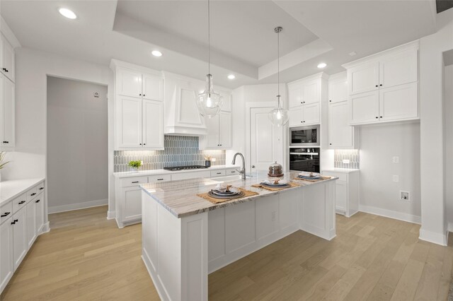 kitchen featuring custom exhaust hood, oven, stainless steel microwave, a sink, and a tray ceiling