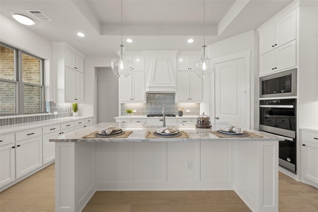 kitchen featuring a center island with sink, a raised ceiling, visible vents, appliances with stainless steel finishes, and custom exhaust hood