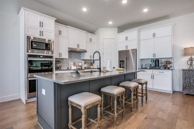 kitchen with appliances with stainless steel finishes, a kitchen island with sink, and white cabinets