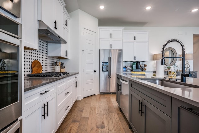 kitchen featuring sink, tasteful backsplash, appliances with stainless steel finishes, light hardwood / wood-style floors, and white cabinets