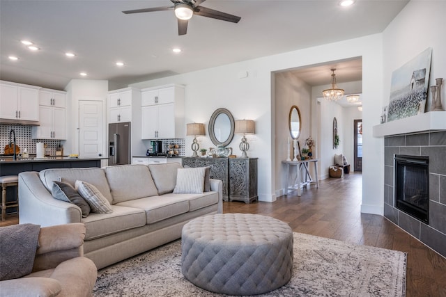 living room with dark wood-type flooring, a fireplace, and ceiling fan with notable chandelier