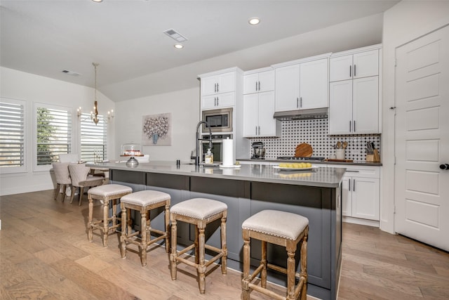 kitchen featuring stainless steel appliances, an island with sink, hanging light fixtures, and white cabinets