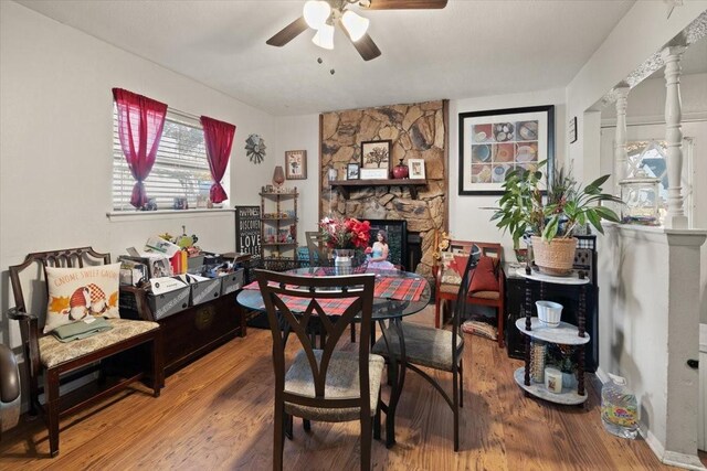 dining space with hardwood / wood-style flooring, ceiling fan, a stone fireplace, and decorative columns