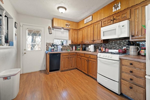 kitchen with a textured ceiling, light wood-type flooring, white appliances, and backsplash