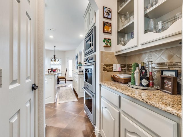 kitchen with appliances with stainless steel finishes, backsplash, dark tile patterned flooring, white cabinetry, and hanging light fixtures