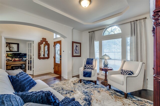 living room with an inviting chandelier, ornamental molding, dark wood-type flooring, and a tray ceiling