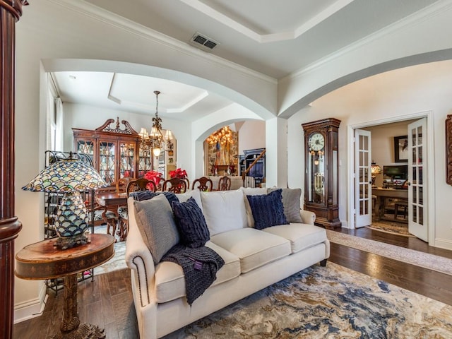 living room featuring hardwood / wood-style flooring, a raised ceiling, crown molding, and a chandelier