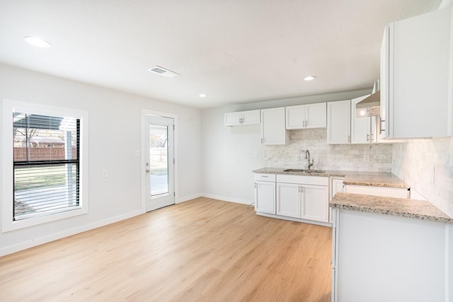 kitchen with light stone countertops, backsplash, sink, light hardwood / wood-style flooring, and white cabinets