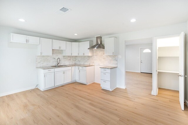 kitchen with decorative backsplash, sink, wall chimney range hood, white cabinets, and light hardwood / wood-style floors