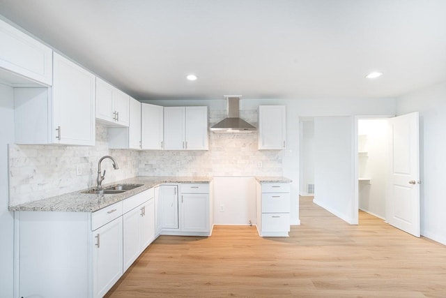 kitchen featuring sink, white cabinets, wall chimney range hood, and light hardwood / wood-style flooring