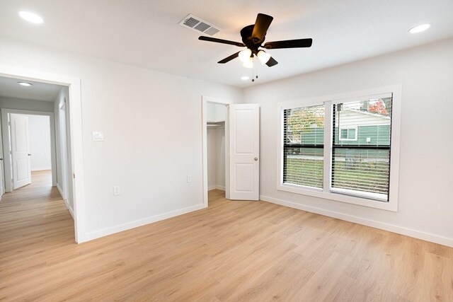 unfurnished bedroom featuring a walk in closet, light wood-type flooring, a closet, and ceiling fan