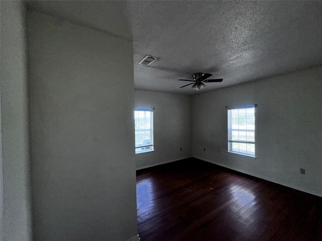 spare room featuring a textured ceiling, plenty of natural light, dark wood-type flooring, and ceiling fan