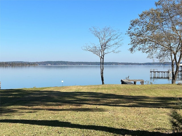 view of dock with a lawn and a water view