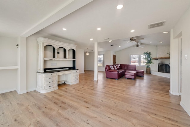 living room featuring a large fireplace, light hardwood / wood-style floors, vaulted ceiling, and ceiling fan