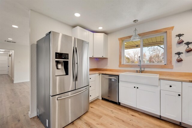 kitchen with hanging light fixtures, sink, appliances with stainless steel finishes, light hardwood / wood-style floors, and white cabinetry