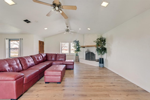 living room with lofted ceiling, light hardwood / wood-style floors, a healthy amount of sunlight, and a large fireplace