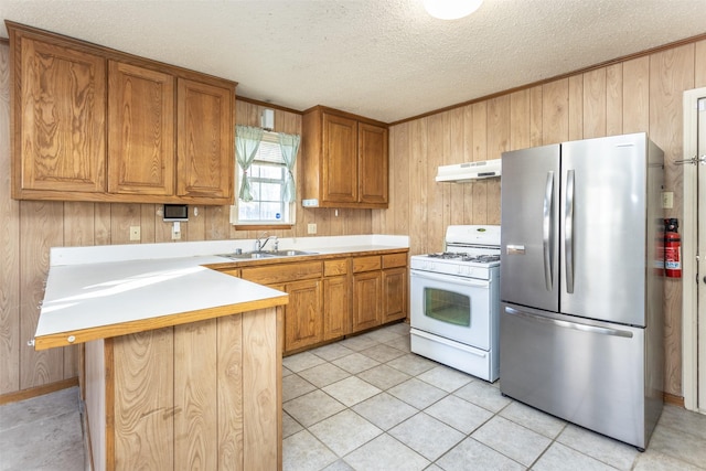 kitchen with a kitchen bar, white gas range, sink, stainless steel refrigerator, and wood walls