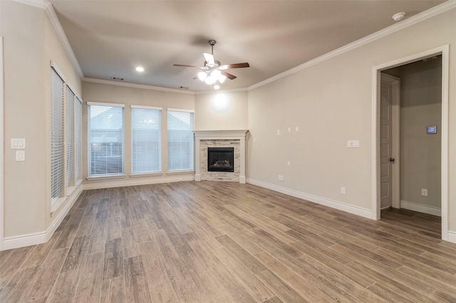 unfurnished living room with hardwood / wood-style flooring, ornamental molding, a stone fireplace, and ceiling fan