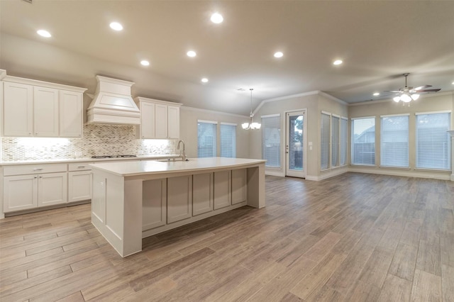 kitchen featuring gas stovetop, a kitchen island with sink, white cabinets, and custom exhaust hood