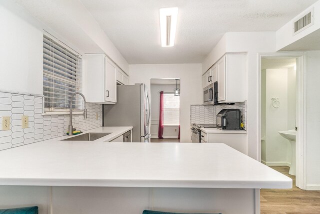 kitchen with kitchen peninsula, appliances with stainless steel finishes, white cabinetry, and sink