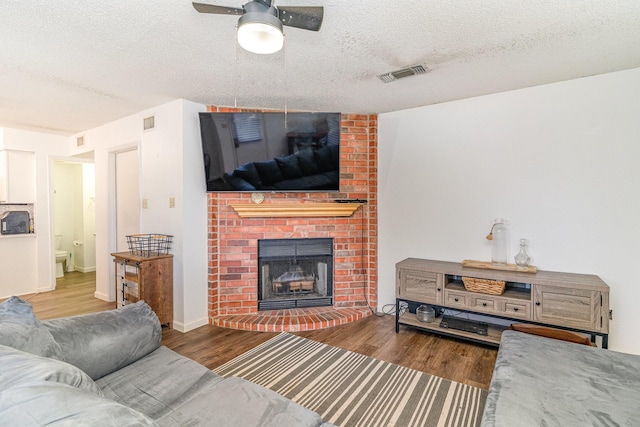 living room with a fireplace, ceiling fan, wood-type flooring, and a textured ceiling