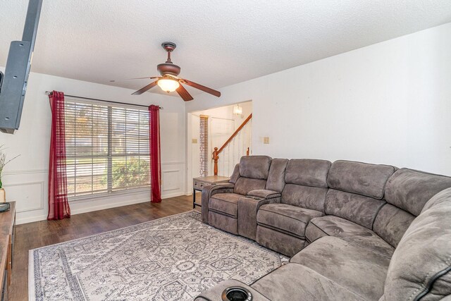 living room with a textured ceiling, ceiling fan, and dark wood-type flooring