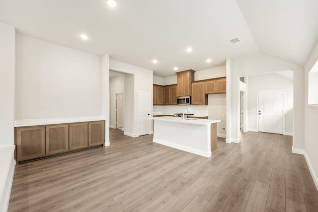 kitchen with brown cabinetry, a sink, light wood-style floors, and stainless steel microwave