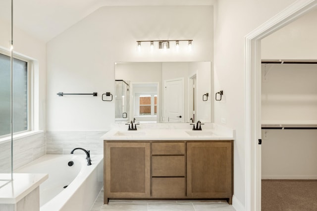 bathroom featuring a walk in closet, a wealth of natural light, a sink, and a garden tub