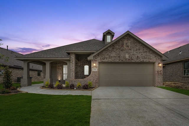 french provincial home featuring a front yard, roof with shingles, brick siding, concrete driveway, and an attached garage