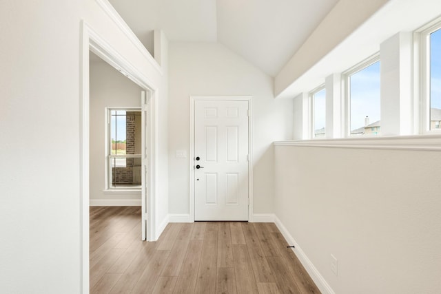 interior space featuring light wood-type flooring, baseboards, and vaulted ceiling