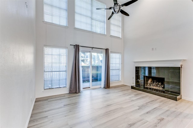 unfurnished living room featuring a tile fireplace, ceiling fan, a high ceiling, and light wood-type flooring