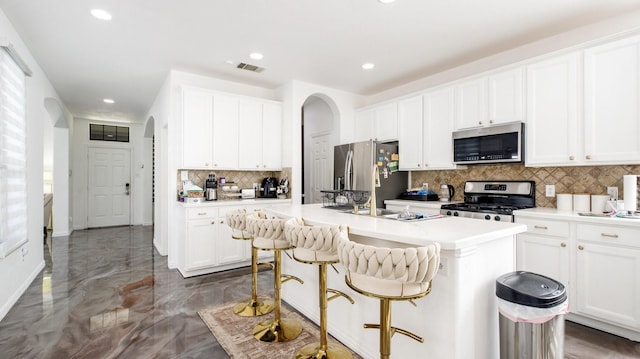 kitchen featuring white cabinetry, a kitchen bar, decorative backsplash, stainless steel appliances, and a center island with sink