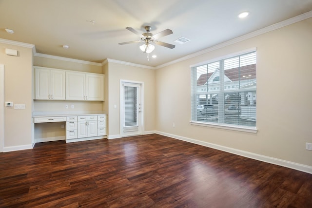 kitchen with dark wood-type flooring, ceiling fan, built in desk, ornamental molding, and white cabinetry