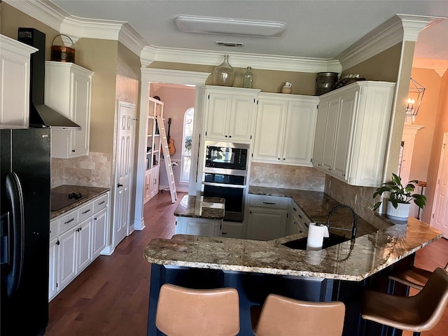 kitchen with black appliances, white cabinets, crown molding, dark hardwood / wood-style floors, and wall chimney exhaust hood