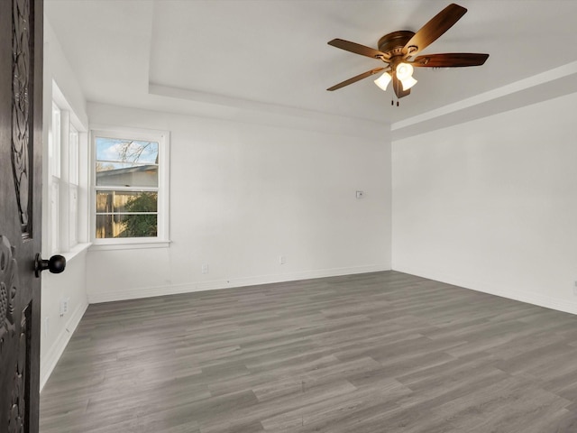 empty room featuring dark wood-type flooring, ceiling fan, and a raised ceiling