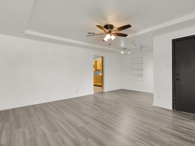 unfurnished living room with a raised ceiling, ceiling fan, built in features, and light hardwood / wood-style floors