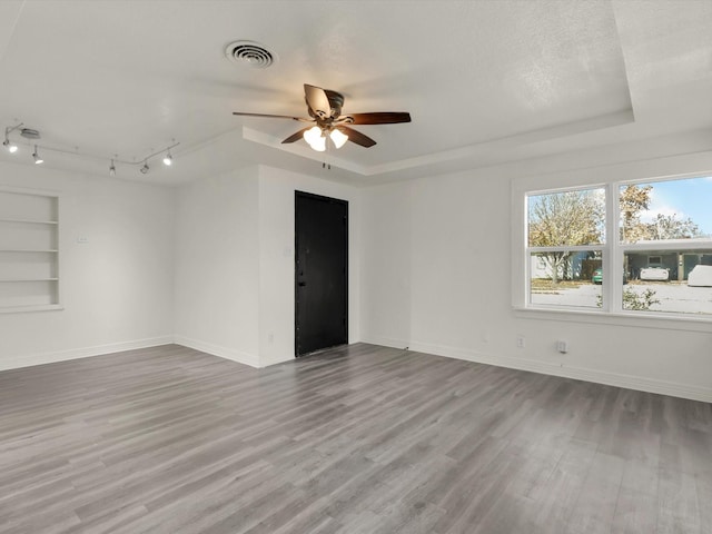 unfurnished room with ceiling fan, light hardwood / wood-style floors, a textured ceiling, built in shelves, and a raised ceiling