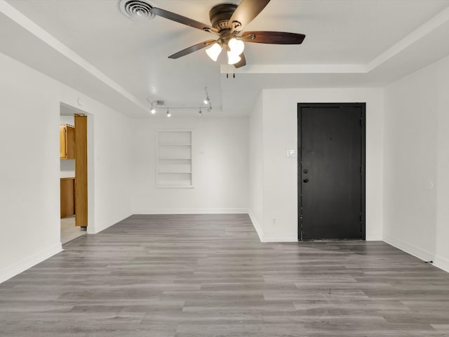 empty room with ceiling fan, a tray ceiling, light wood-type flooring, and built in shelves