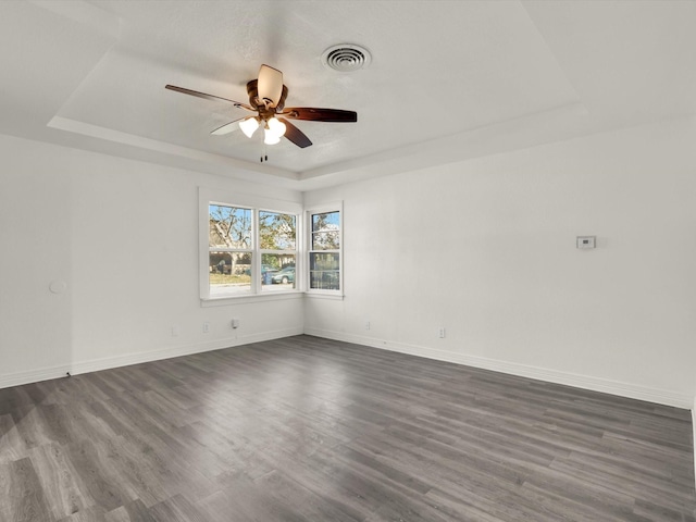 empty room featuring dark wood-type flooring, a raised ceiling, and ceiling fan