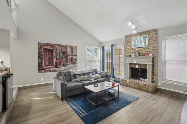 living room featuring high vaulted ceiling, wood-type flooring, a textured ceiling, and a brick fireplace