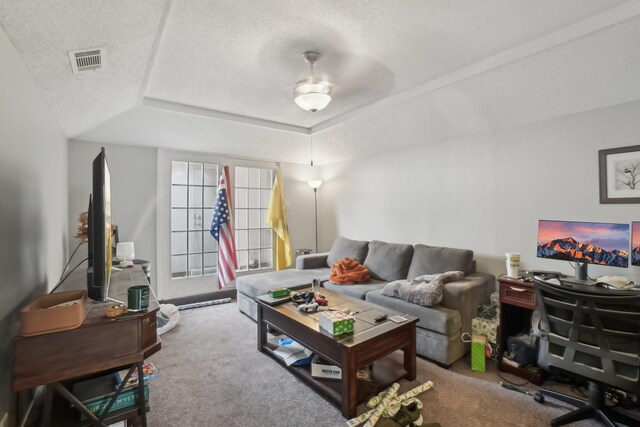 carpeted living room with a textured ceiling, a raised ceiling, and ceiling fan