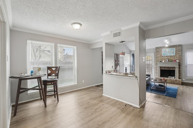 kitchen with light hardwood / wood-style flooring, hanging light fixtures, a textured ceiling, and a brick fireplace