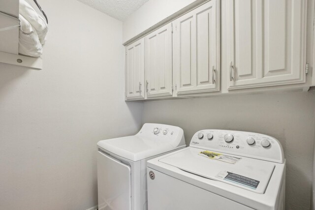 laundry room featuring washer and clothes dryer, cabinets, and a textured ceiling