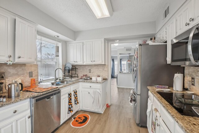 kitchen with light hardwood / wood-style floors, white cabinetry, backsplash, and appliances with stainless steel finishes