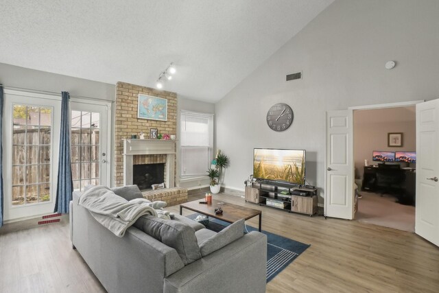 living room featuring a textured ceiling, light hardwood / wood-style floors, a fireplace, and high vaulted ceiling