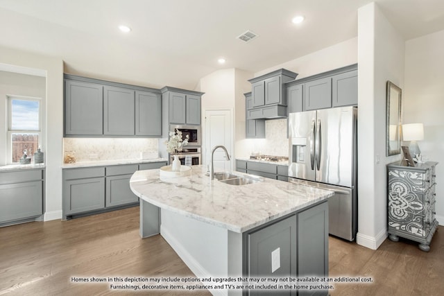 kitchen with gray cabinets, appliances with stainless steel finishes, sink, a kitchen island with sink, and light stone countertops