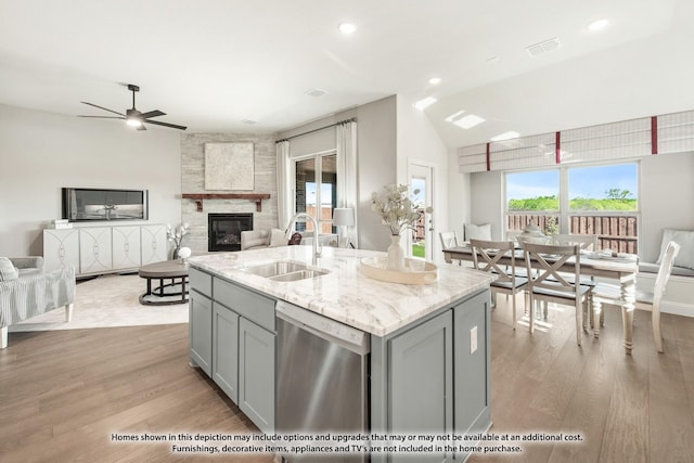 kitchen featuring sink, gray cabinetry, stainless steel dishwasher, an island with sink, and a fireplace