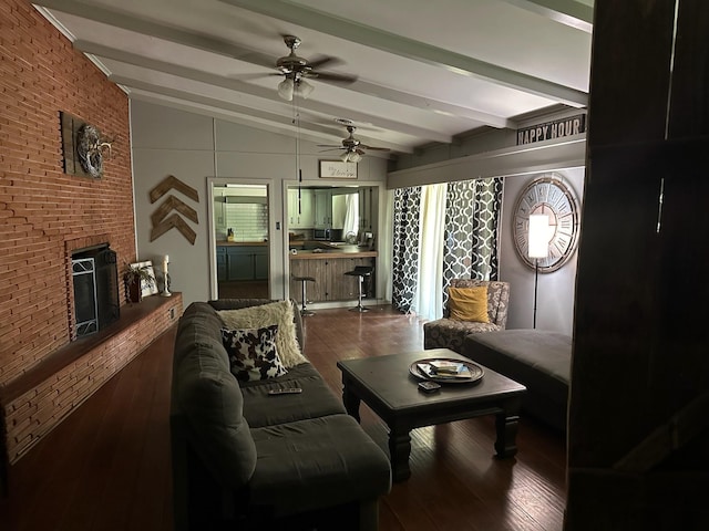 living room featuring vaulted ceiling with beams, a brick fireplace, ceiling fan, and dark wood-type flooring