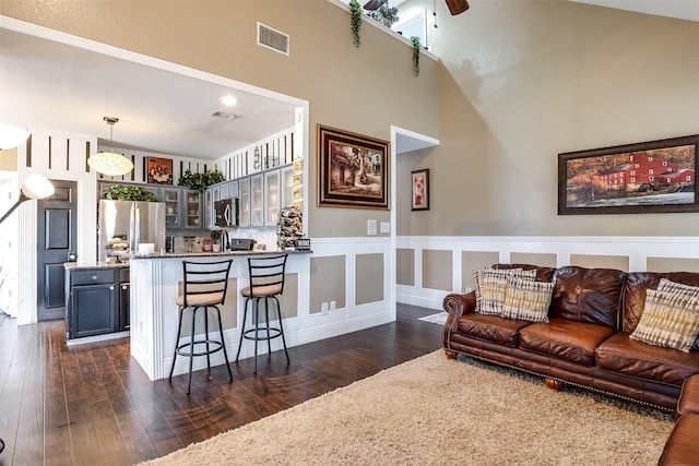 living room with a high ceiling, dark wood-type flooring, and ceiling fan