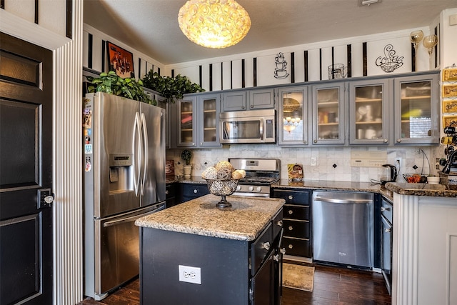 kitchen with a center island, hanging light fixtures, stainless steel appliances, light stone countertops, and backsplash